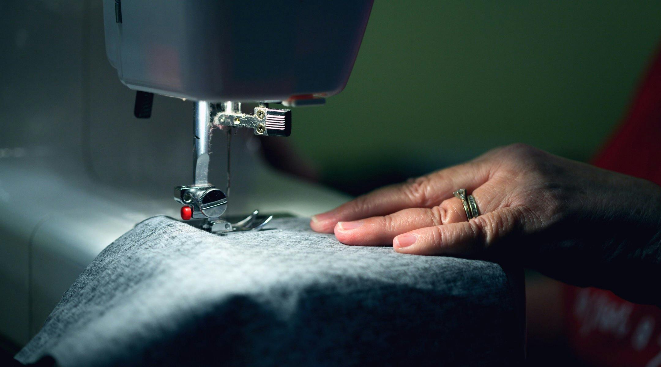 En hånd som dytter et tekstil gjennom en symaskin